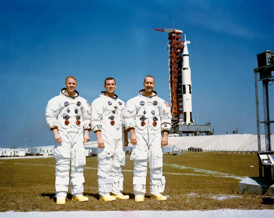 These three astronauts are the prime crew of the Apollo 9 Earth-orbital space mission. Left to right, are Russell L. Schweickart, lunar module pilot; David R. Scott, command module pilot; and James A. McDivitt, commander. In the right background is the Apollo 9 space vehicle on Pad A, Launch Complex 39, Kennedy Space Center (KSC).
