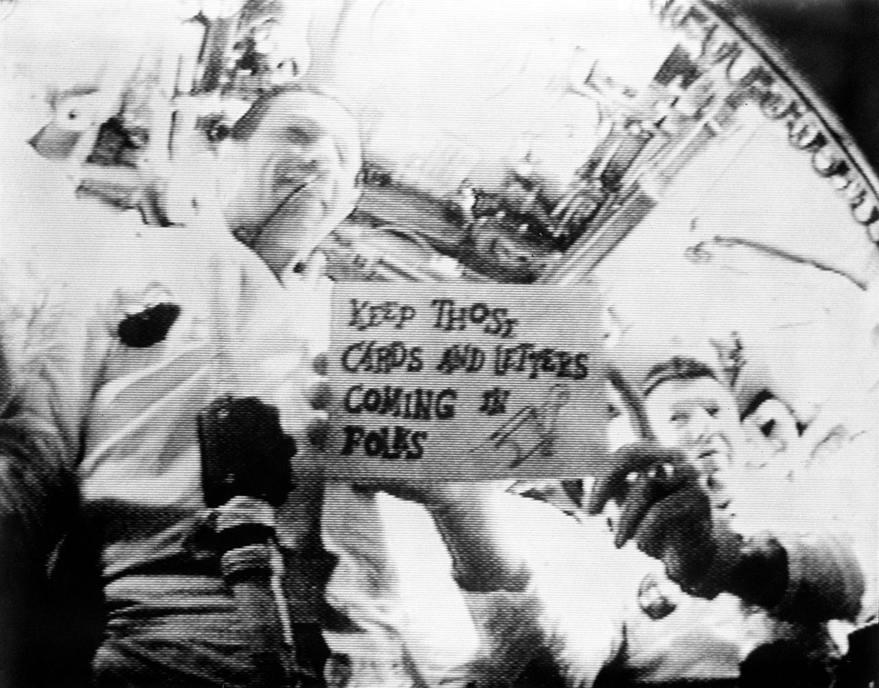 Apollo 7 astronauts seen in the first live television transmission from space. Sign reads “Keep those cards and letters coming in folks.”